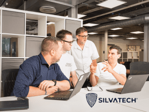 Silvatech team of four men discussing work around a desk with two laptops