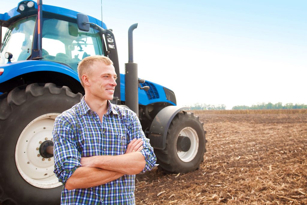 A farm standing besides his tractor.